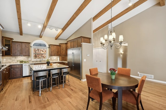 kitchen with a kitchen island, decorative light fixtures, rail lighting, appliances with stainless steel finishes, and tasteful backsplash