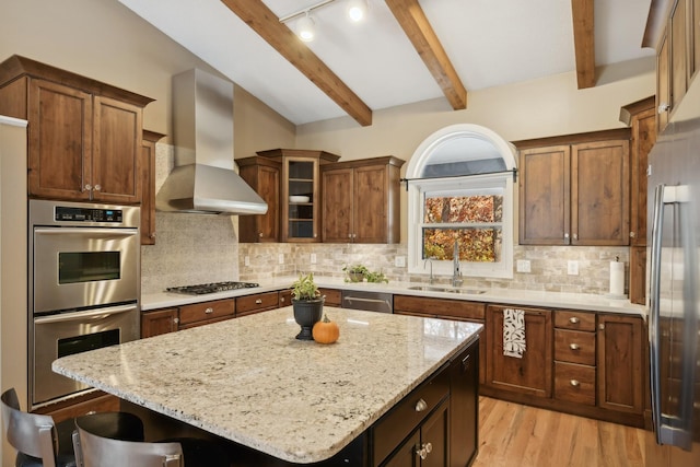 kitchen featuring beam ceiling, stainless steel appliances, wall chimney exhaust hood, and tasteful backsplash