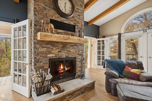 living room featuring light hardwood / wood-style floors, a healthy amount of sunlight, beamed ceiling, and a fireplace