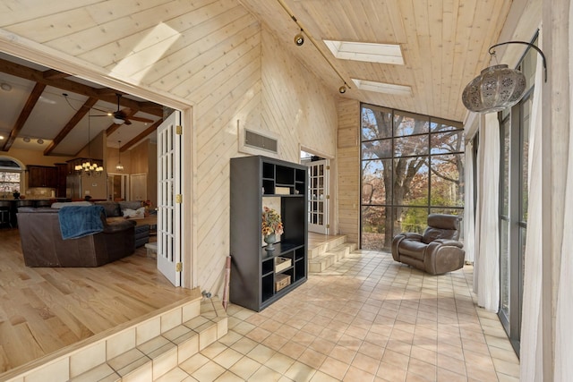 interior space featuring high vaulted ceiling, beamed ceiling, ceiling fan with notable chandelier, a skylight, and light hardwood / wood-style floors