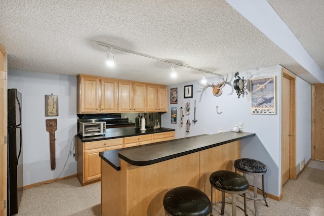 kitchen with kitchen peninsula, a textured ceiling, track lighting, and black refrigerator