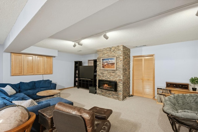 living room with a stone fireplace, a textured ceiling, carpet, and rail lighting