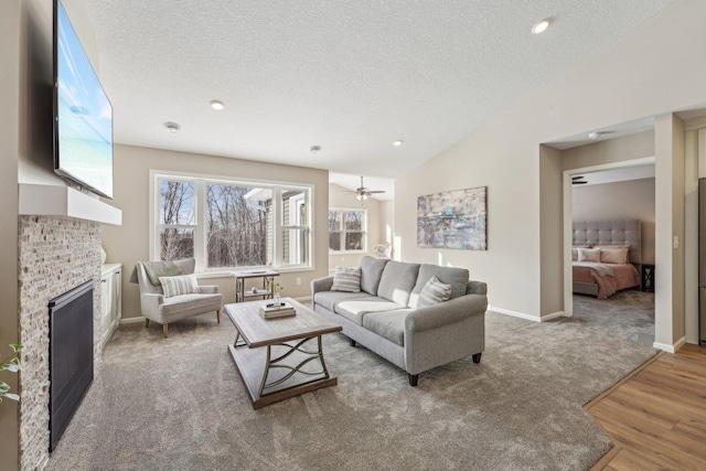 living room featuring ceiling fan, a stone fireplace, wood-type flooring, vaulted ceiling, and a textured ceiling