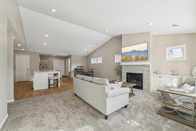 living room featuring a fireplace, light hardwood / wood-style flooring, lofted ceiling, and sink