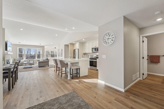 interior space with a textured ceiling, lofted ceiling, sink, and light hardwood / wood-style flooring