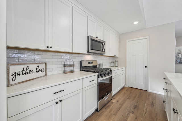 kitchen featuring white cabinetry, stainless steel appliances, tasteful backsplash, light stone counters, and light wood-type flooring