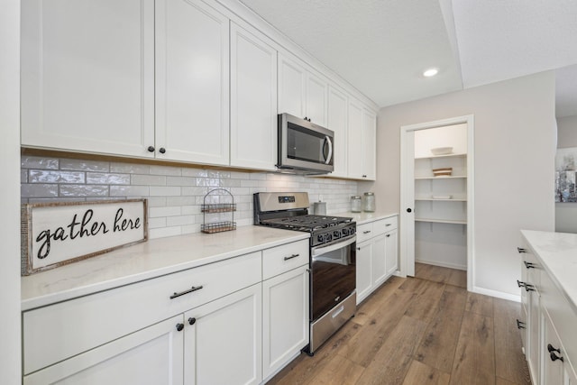 kitchen with white cabinetry, tasteful backsplash, light stone counters, appliances with stainless steel finishes, and light wood-type flooring