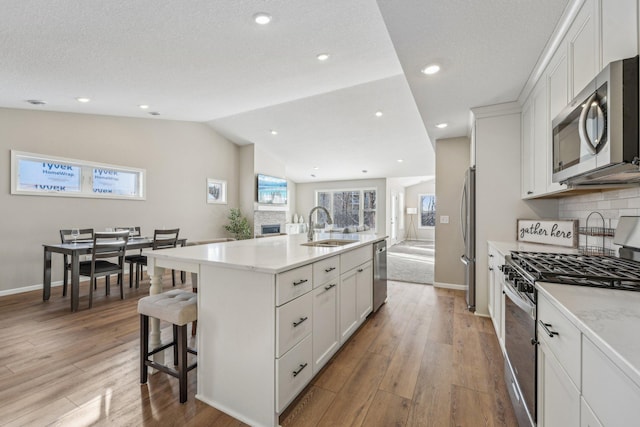 kitchen featuring white cabinetry, sink, stainless steel appliances, lofted ceiling, and a center island with sink