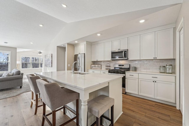 kitchen with a kitchen bar, backsplash, stainless steel appliances, a kitchen island with sink, and lofted ceiling