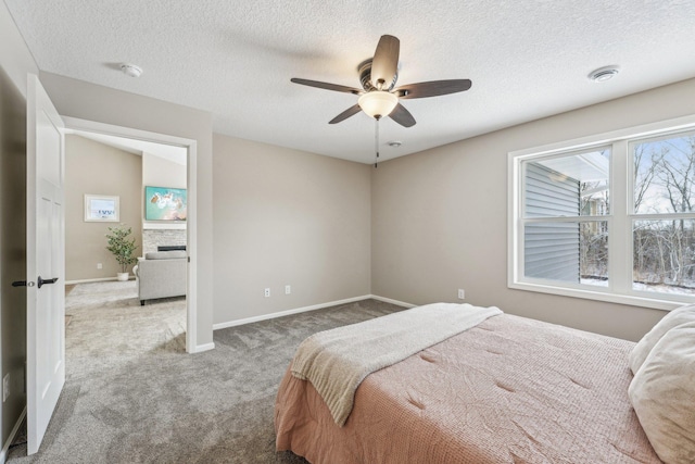 carpeted bedroom with a textured ceiling, a stone fireplace, and ceiling fan