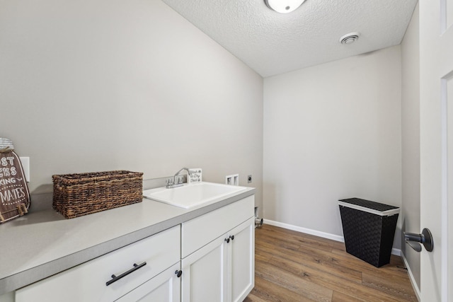 washroom with cabinets, hookup for an electric dryer, a textured ceiling, sink, and light hardwood / wood-style flooring