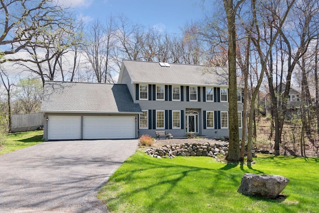 colonial inspired home featuring fence, an attached garage, driveway, and a front lawn