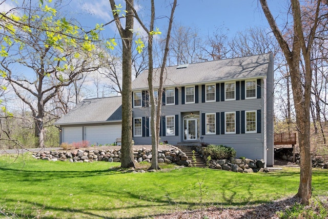 colonial home featuring a shingled roof, a front yard, and a garage