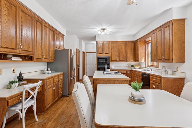 kitchen featuring a center island with sink, a sink, light countertops, black appliances, and light wood-style flooring