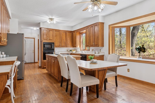kitchen featuring brown cabinetry, light countertops, light wood finished floors, and black appliances