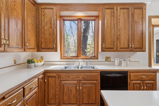 kitchen with brown cabinetry, a sink, black dishwasher, and light countertops