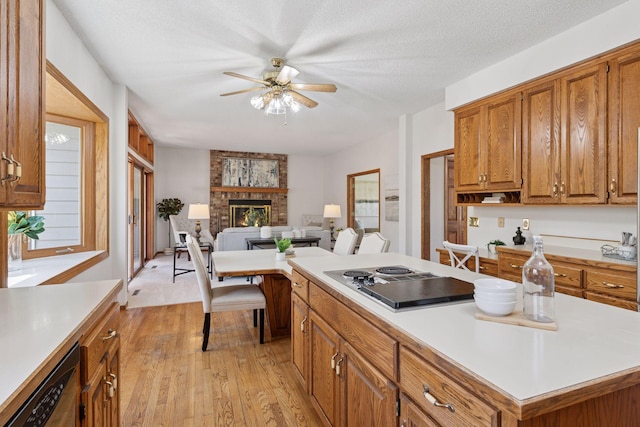 kitchen with stainless steel dishwasher, brown cabinetry, a fireplace, ceiling fan, and stovetop with downdraft
