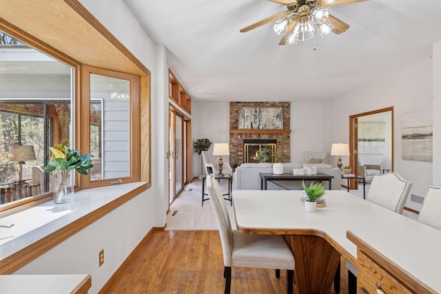 dining area featuring a ceiling fan, light wood-style flooring, and a brick fireplace