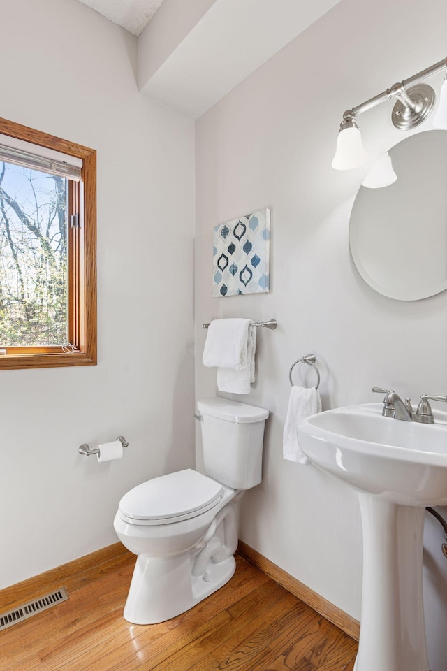 half bath featuring a sink, toilet, baseboards, wood finished floors, and visible vents