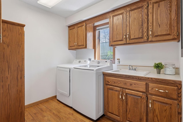 laundry room featuring baseboards, washer and clothes dryer, a sink, cabinet space, and light wood finished floors