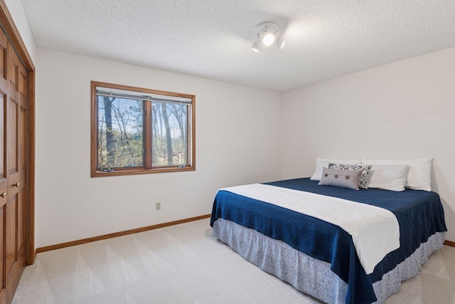 bedroom featuring baseboards, a textured ceiling, a closet, and light carpet
