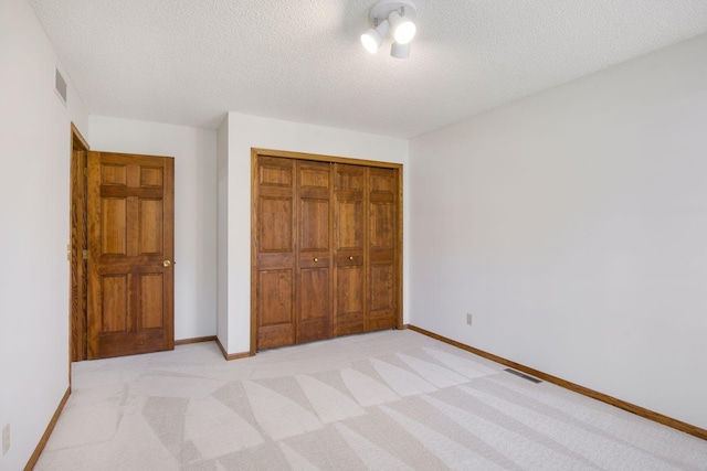 unfurnished bedroom featuring a textured ceiling, visible vents, light carpet, and a closet
