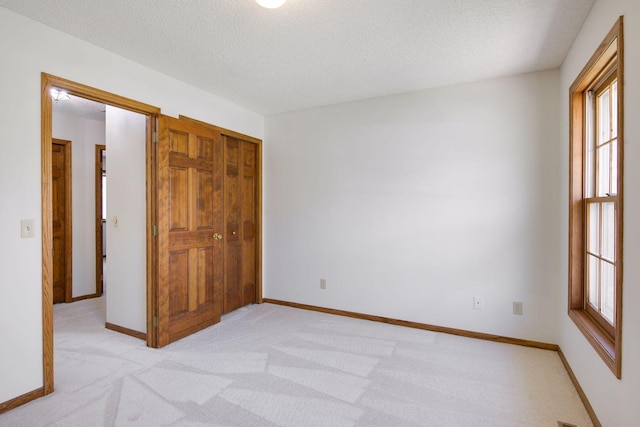 unfurnished bedroom with multiple windows, a closet, a textured ceiling, and light colored carpet