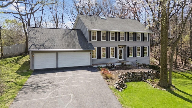 colonial-style house with an attached garage, driveway, roof with shingles, and a front lawn