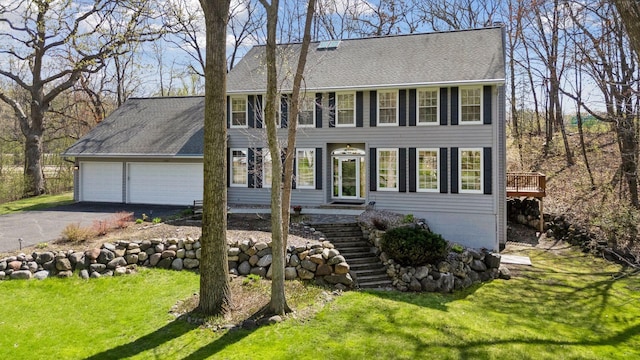 colonial home with roof with shingles, driveway, a front yard, and a garage