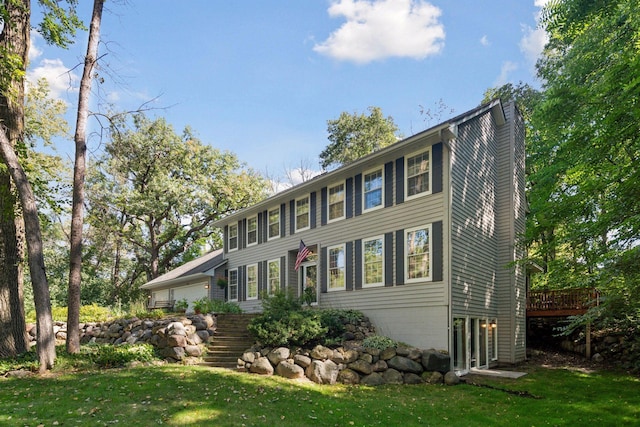 colonial inspired home featuring a wooden deck, a chimney, stairway, and a front yard