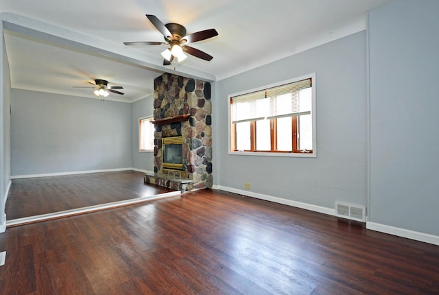 unfurnished living room featuring dark hardwood / wood-style flooring, ceiling fan, and a stone fireplace