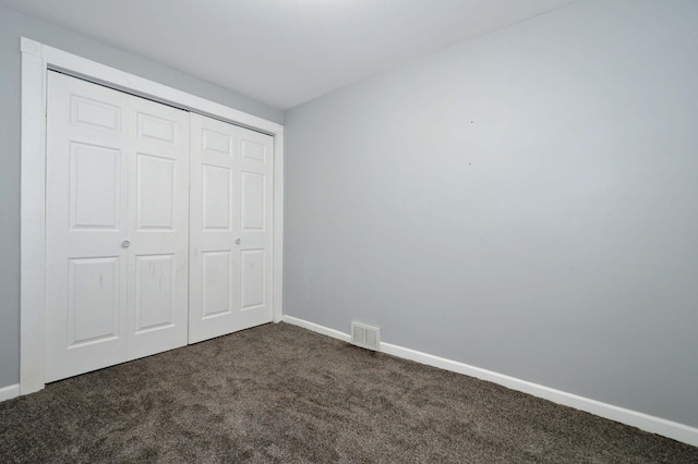 unfurnished bedroom featuring dark carpet and a closet