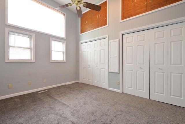 unfurnished bedroom featuring carpet floors, a high ceiling, two closets, and ceiling fan