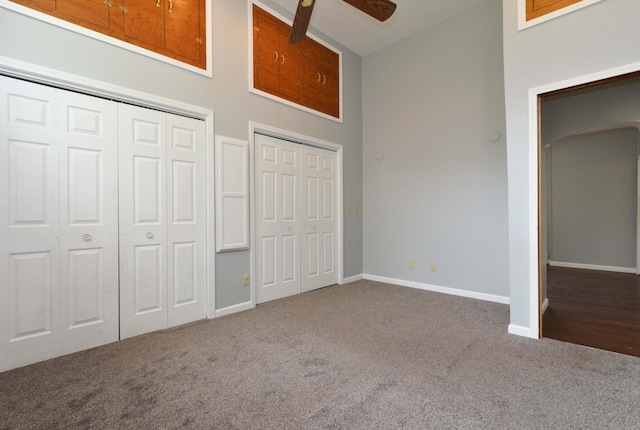 unfurnished bedroom with ceiling fan, two closets, carpet, and a towering ceiling