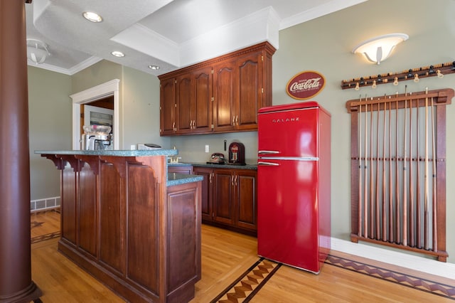 kitchen with a breakfast bar area, crown molding, light wood-type flooring, and fridge