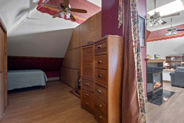 bedroom with wood-type flooring, ceiling fan, a tile fireplace, and vaulted ceiling