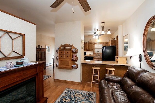 living room with baseboard heating, sink, light hardwood / wood-style floors, and ceiling fan