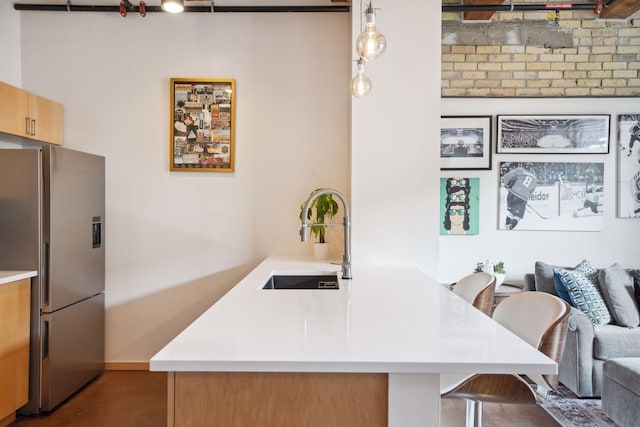 kitchen with kitchen peninsula, stainless steel fridge, hanging light fixtures, a kitchen breakfast bar, and sink