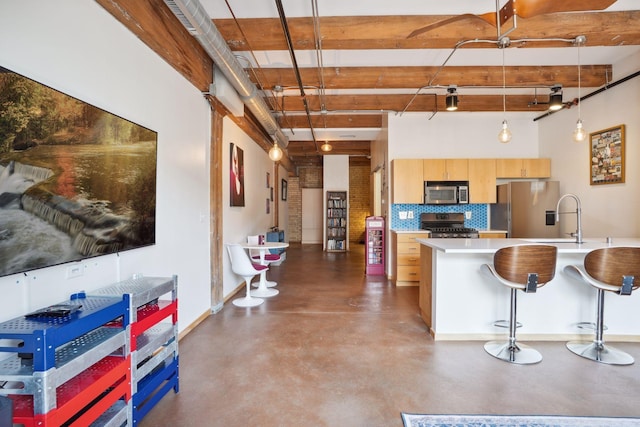 kitchen featuring light brown cabinets, a breakfast bar area, hanging light fixtures, appliances with stainless steel finishes, and tasteful backsplash