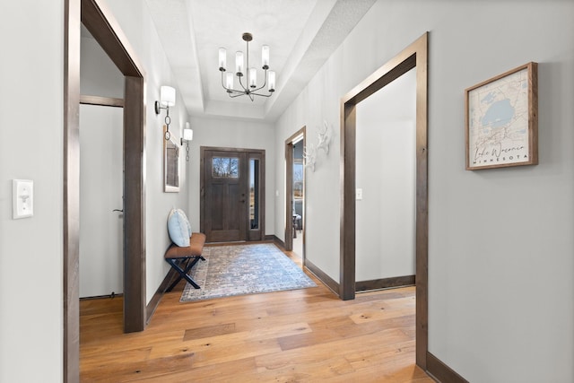 entrance foyer featuring an inviting chandelier, light wood-type flooring, and a raised ceiling