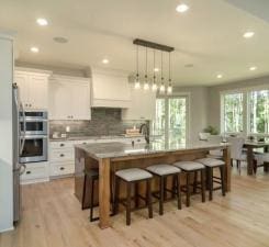 kitchen featuring light hardwood / wood-style flooring, a kitchen island with sink, white cabinetry, and appliances with stainless steel finishes