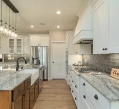 kitchen featuring hanging light fixtures, tasteful backsplash, white cabinetry, and custom range hood