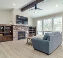 living room with a fireplace, light hardwood / wood-style floors, vaulted ceiling with beams, and plenty of natural light