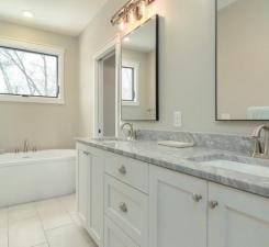 bathroom featuring a healthy amount of sunlight, tile flooring, a washtub, and double sink vanity