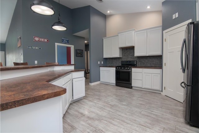 kitchen featuring stainless steel refrigerator, hanging light fixtures, stove, tasteful backsplash, and white cabinets