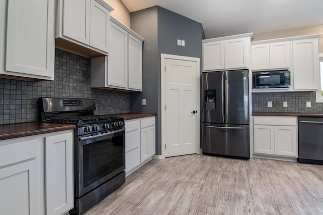 kitchen with appliances with stainless steel finishes, white cabinetry, tasteful backsplash, and light hardwood / wood-style floors