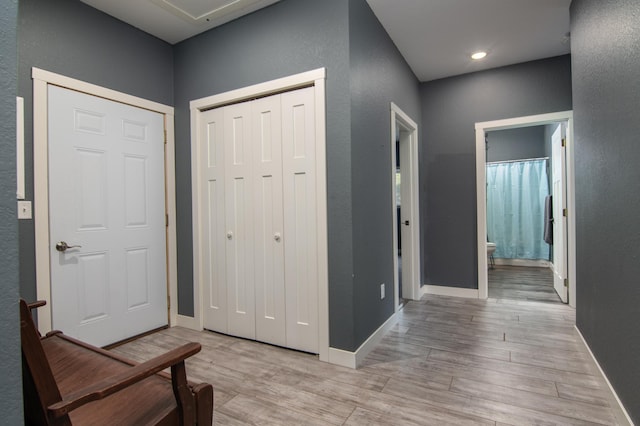 foyer featuring light wood-style floors, a textured wall, and baseboards