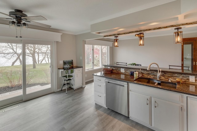 kitchen with hanging light fixtures, dark stone counters, sink, white cabinetry, and stainless steel dishwasher