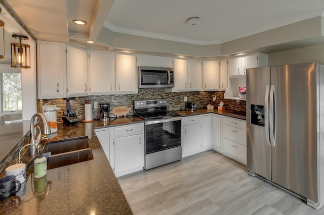 kitchen featuring stainless steel appliances, dark stone counters, ornamental molding, sink, and white cabinetry