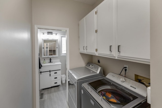 washroom with sink, washing machine and dryer, light hardwood / wood-style floors, and cabinets